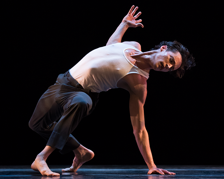 the dancer in another crouched positing leaning to his left supported by his left arm and both legs... his arm muscles and the muscles of his neck are prominent
